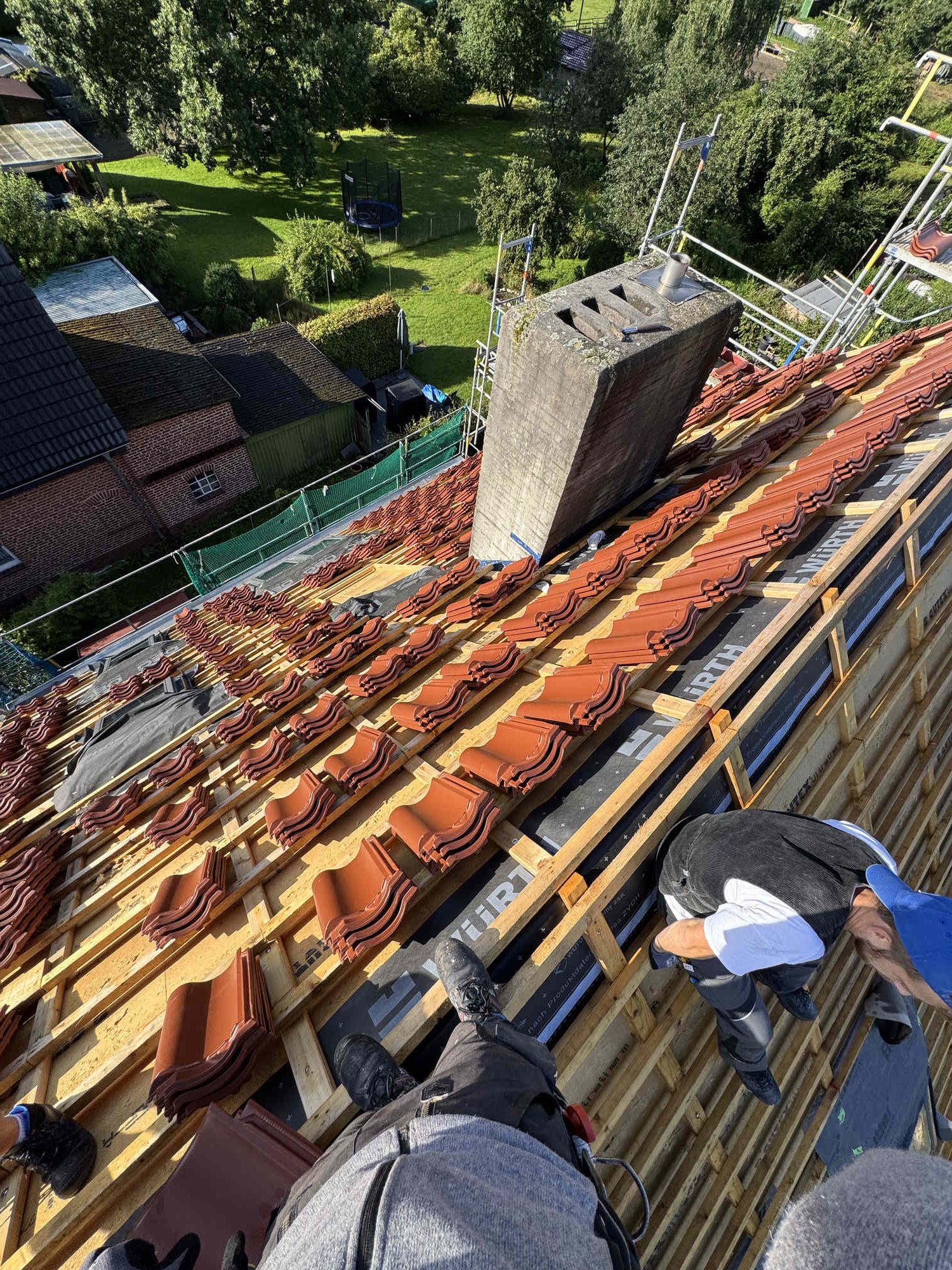 Blick über die frisch eingedeckte Dachfläche mit verteilten Dachpfannen und Schornstein