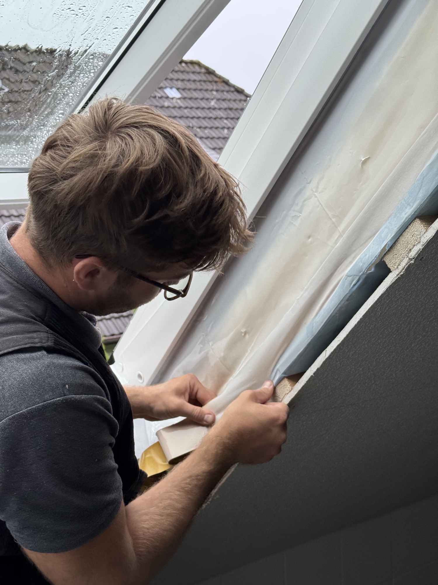 Zimmerer verklebt die Luftdichtungsbahn am neuen Fenster