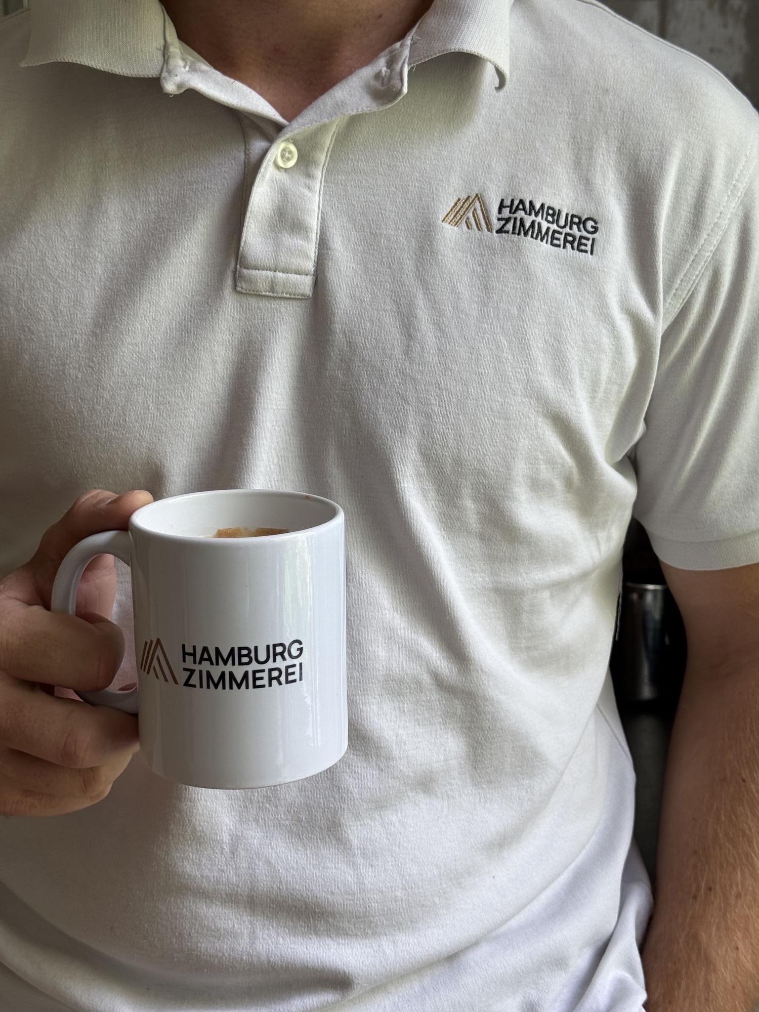 Poloshirt und Kaffeetasse mit dem Logo der Hamburg Zimmerei